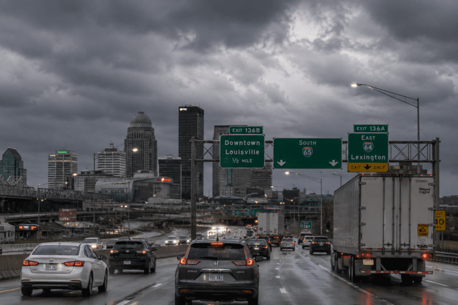 Traffic moving through a Louisville highway corridor with cars and commercial trucks in overcast conditions